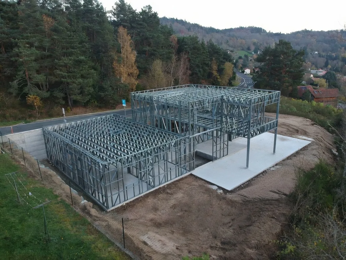 Ossature métallique légère d'une maison montée sur un terrain en pente, avec avancée couverte sur poteaux
