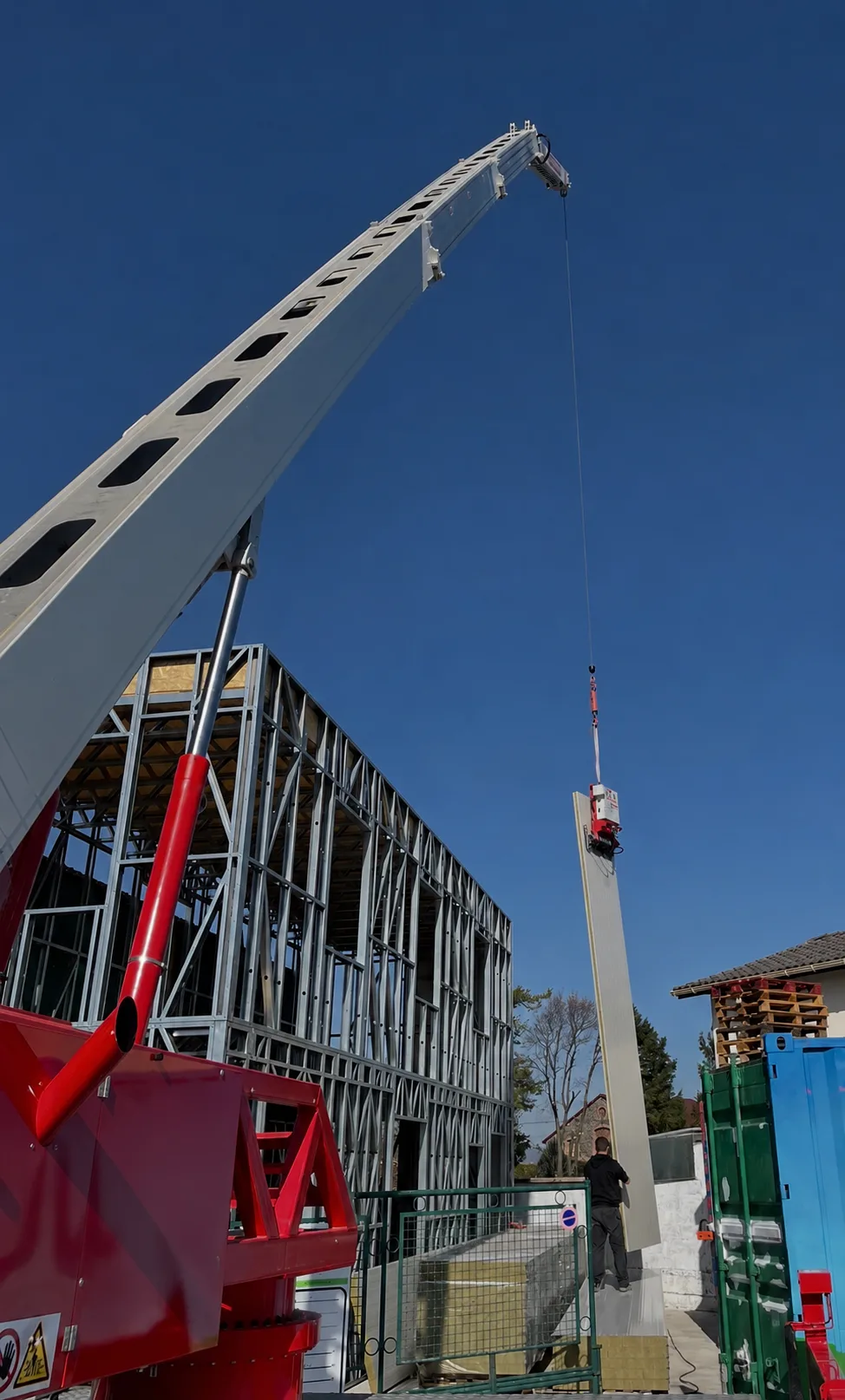 Levage d'un panneau de façade à la grue sur l'ossature métallique légère d'un bâtiment
